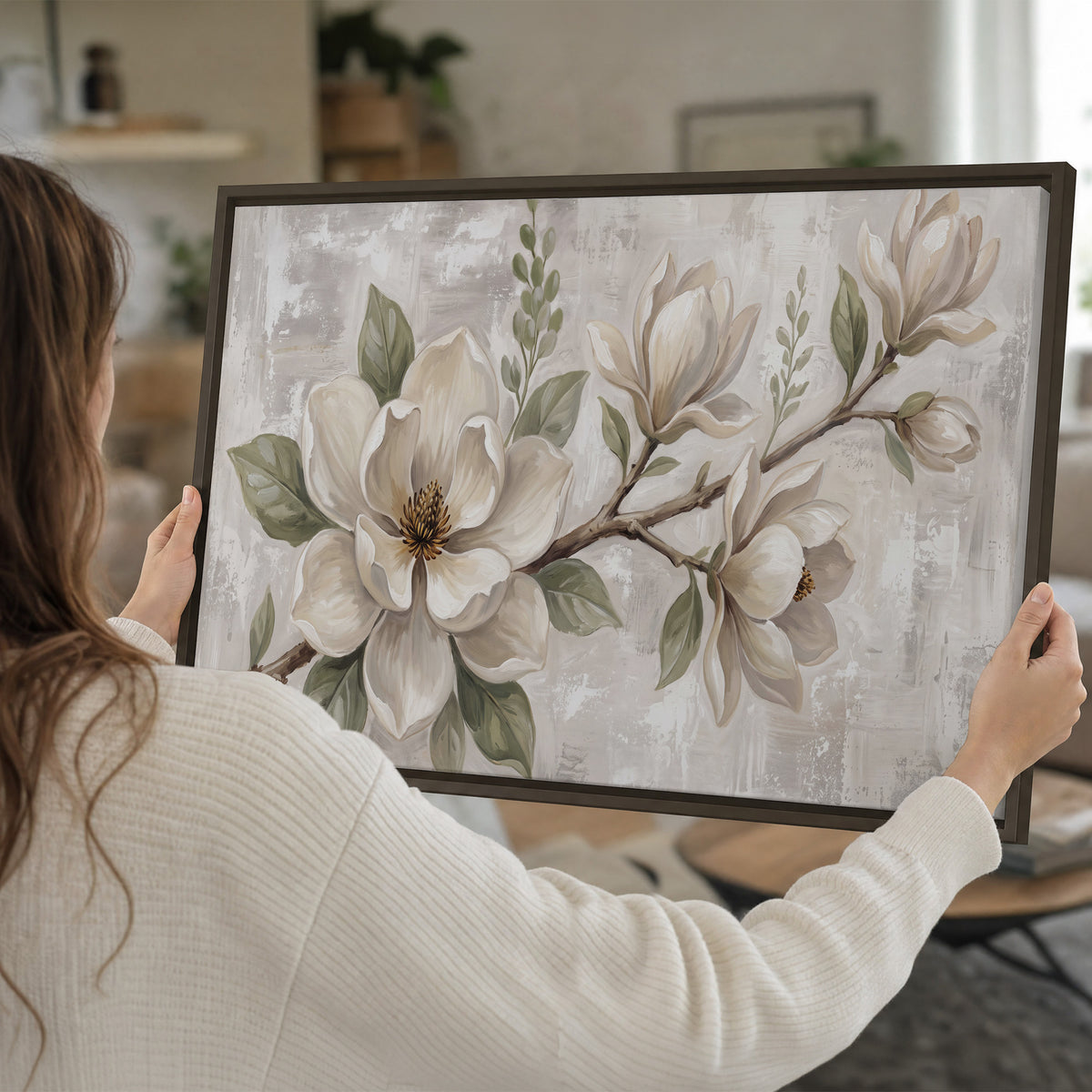 Large ivory magnolia blossoms and soft green leaves on pale gray single framed canvas wall art held in hands