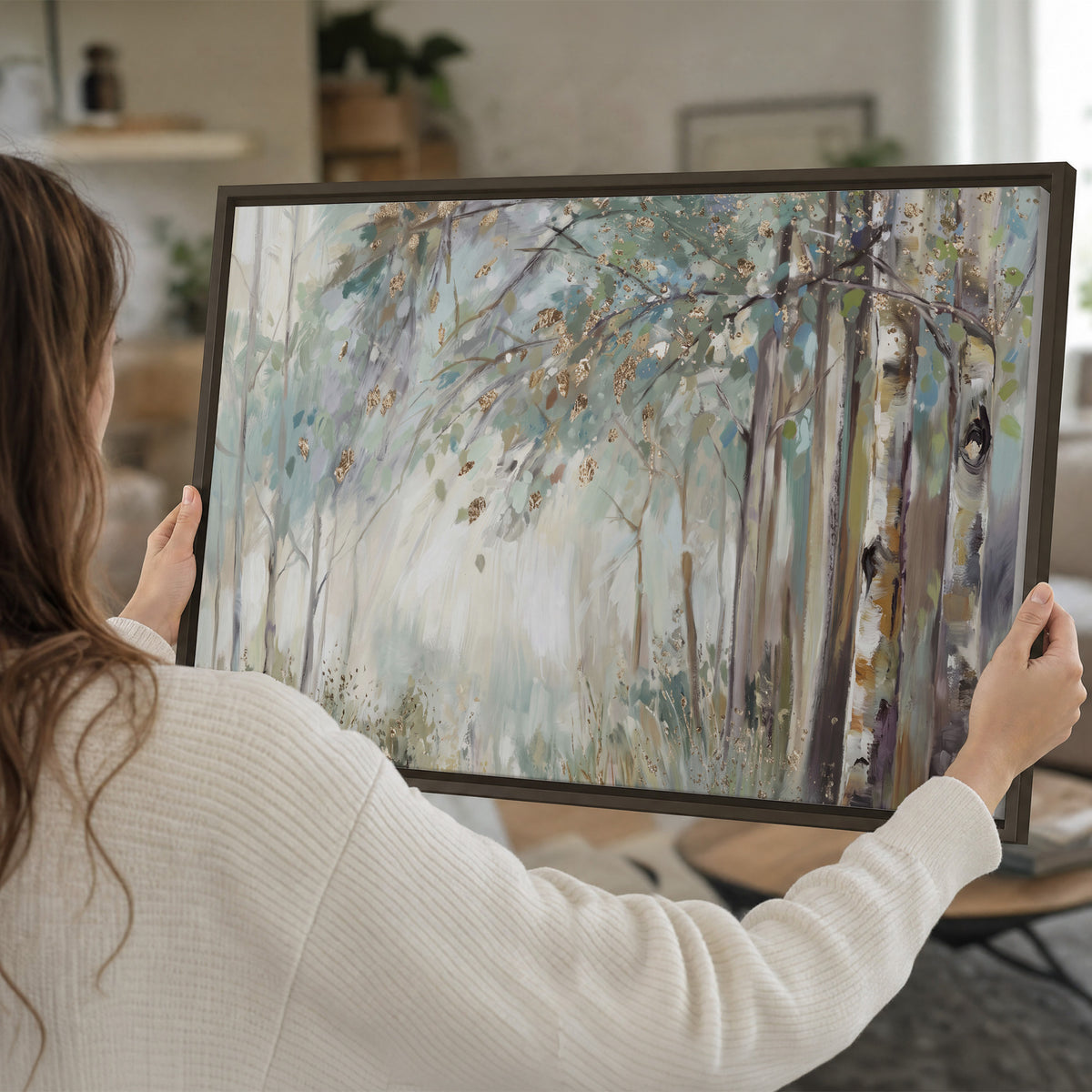Slender woodland trunks and delicate branches in soft green and cream single framed canvas wall art held in hands