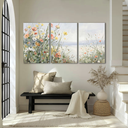 Small colorful wildflowers and light grasses beside a pale lake 3 piece canvas wall art displayed in a entryway