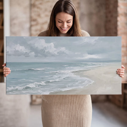 Gentle pale blue waves washing across a light sandy beach single canvas wall art held in hands