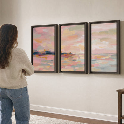Pink, peach and yellow painted-style sky and water reflections 3 piece framed canvas wall art three panel arrangement on a wall