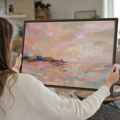 Pink, peach and yellow painted-style sky and water reflections single framed canvas wall art held in hands