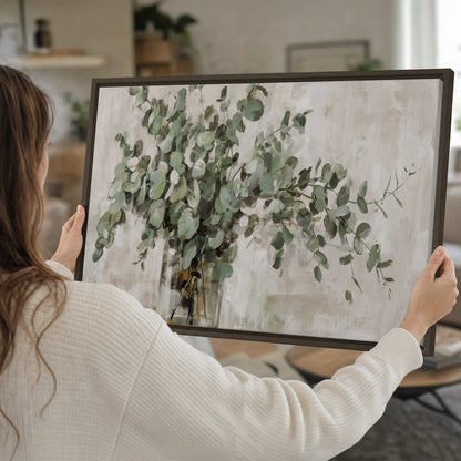 Soft sage eucalyptus leaves and pale stems on a warm cream background single framed canvas wall art held in hands