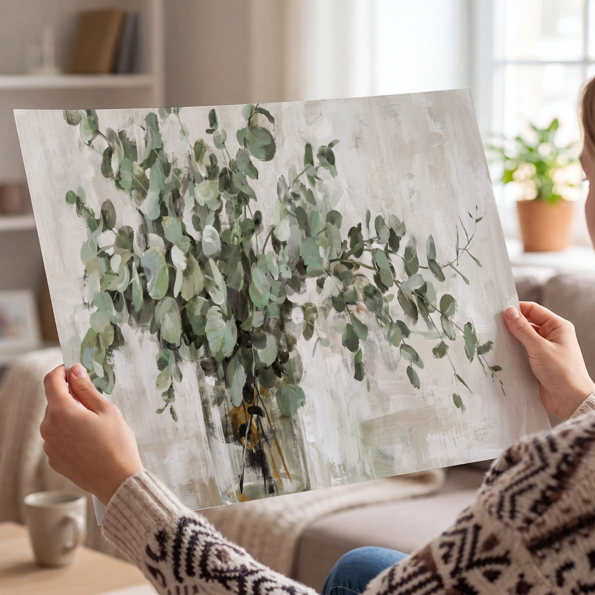 Soft sage eucalyptus leaves and pale stems on a warm cream background single poster print held in hands