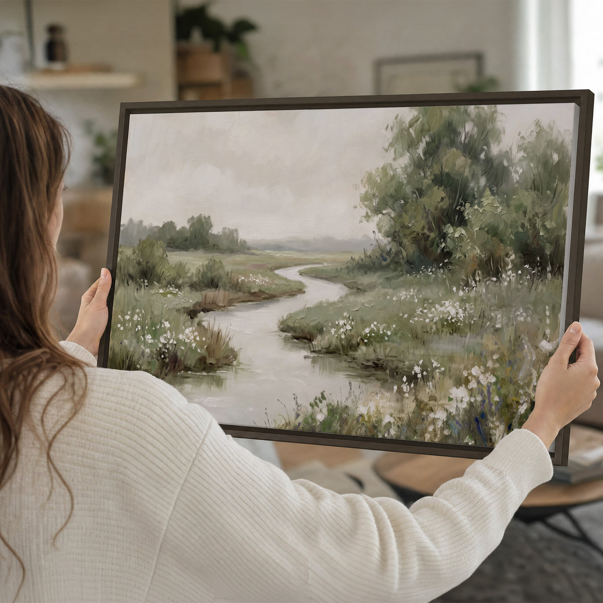 A narrow winding stream through quiet green meadows and trees single framed canvas wall art held in hands