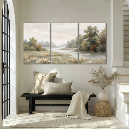 A broad pale river bordered by green trees and small meadow flowers 3 piece canvas wall art displayed in a entryway