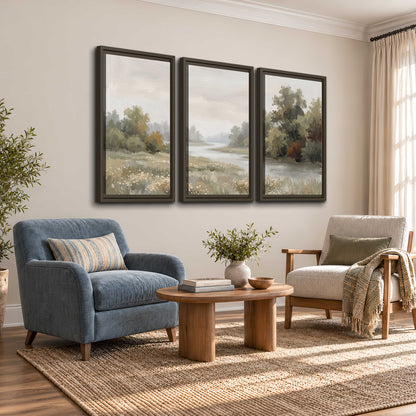 A broad pale river bordered by green trees and small meadow flowers 3 piece framed canvas wall art styled in an interior