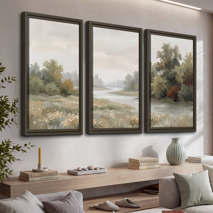 A broad pale river bordered by green trees and small meadow flowers 3 piece framed canvas wall art displayed in a console