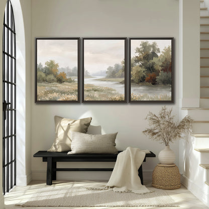 A broad pale river bordered by green trees and small meadow flowers 3 piece framed canvas wall art displayed in a entryway