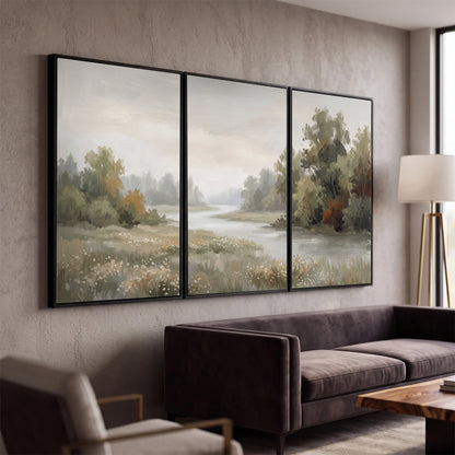 A broad pale river bordered by green trees and small meadow flowers 3 piece framed canvas wall art displayed in a modern living room