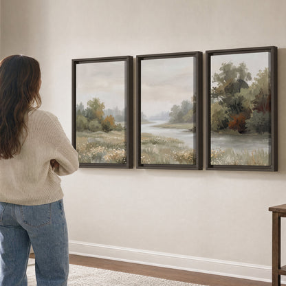 A broad pale river bordered by green trees and small meadow flowers 3 piece framed canvas wall art three panel arrangement on a wall