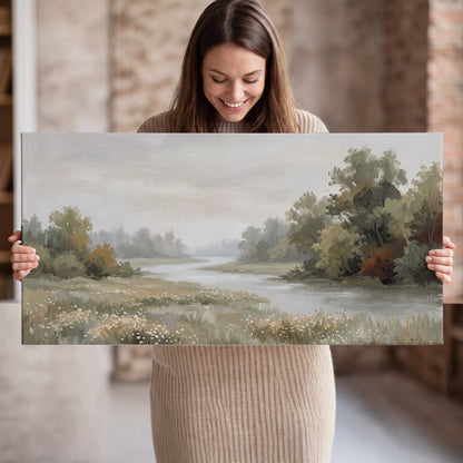 A broad pale river bordered by green trees and small meadow flowers single canvas wall art held in hands