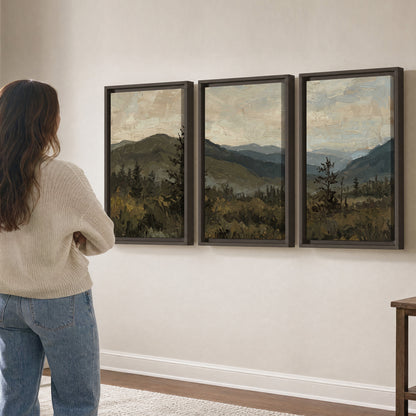 Layered mountain ridges and dark evergreen trees beneath a muted cloudy sky 3 piece framed canvas wall art three panel arrangement on a wall