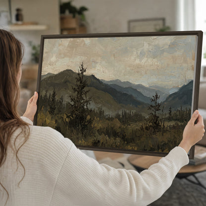 Layered mountain ridges and dark evergreen trees beneath a muted cloudy sky single framed canvas wall art held in hands