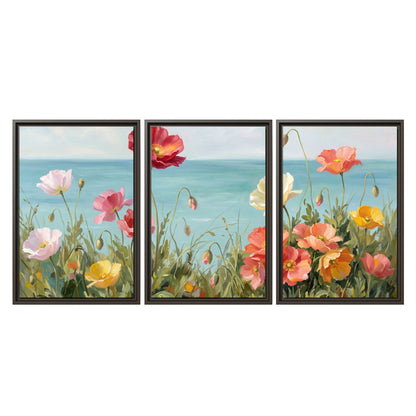 Colorful red, peach and yellow flowers beside a turquoise sea 3 piece framed canvas wall art viewed straight on