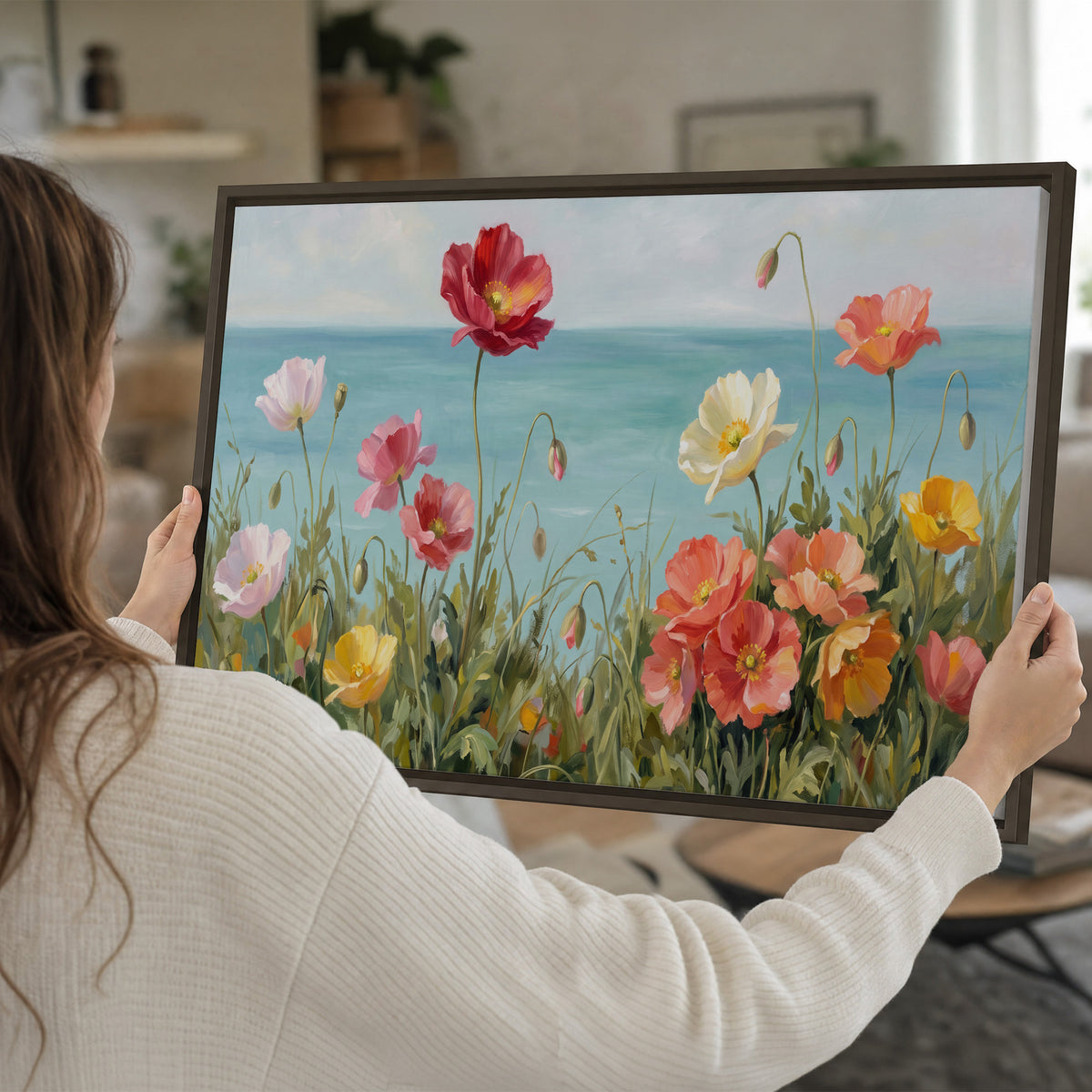 Colorful red, peach and yellow flowers beside a turquoise sea single framed canvas wall art held in hands