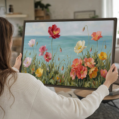 Colorful red, peach and yellow flowers beside a turquoise sea single framed canvas wall art held in hands