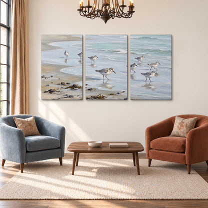 Small shorebirds standing along a pale blue shoreline 3 piece canvas wall art styled in an interior