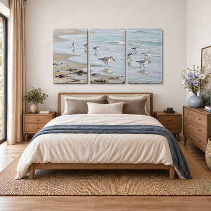 Small shorebirds standing along a pale blue shoreline 3 piece canvas wall art styled in an interior