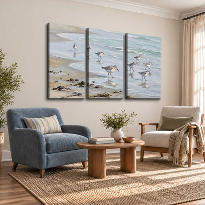 Small shorebirds standing along a pale blue shoreline 3 piece canvas wall art styled in an interior