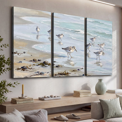 Small shorebirds standing along a pale blue shoreline 3 piece canvas wall art displayed in a console