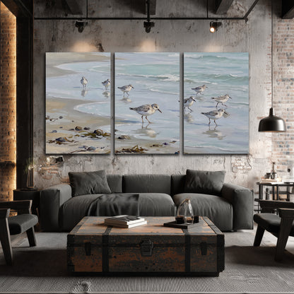 Small shorebirds standing along a pale blue shoreline 3 piece canvas wall art displayed in a industrial room