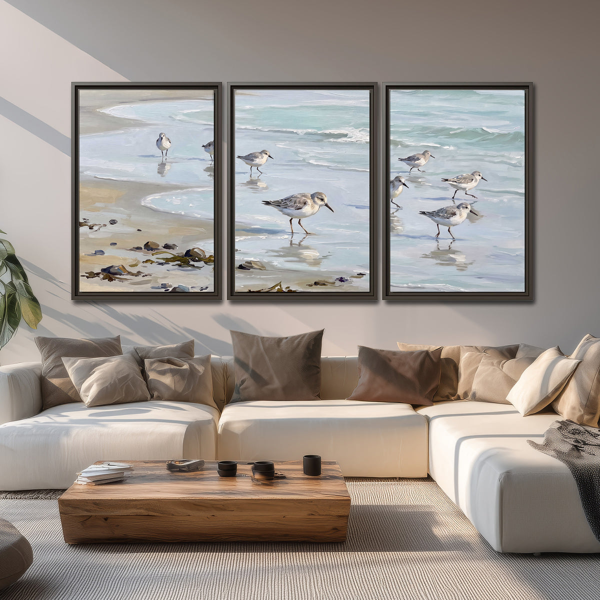 Small shorebirds standing along a pale blue shoreline 3 piece framed canvas wall art displayed in a living room