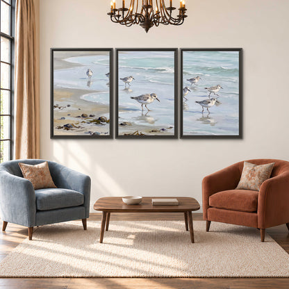 Small shorebirds standing along a pale blue shoreline 3 piece framed canvas wall art styled in an interior