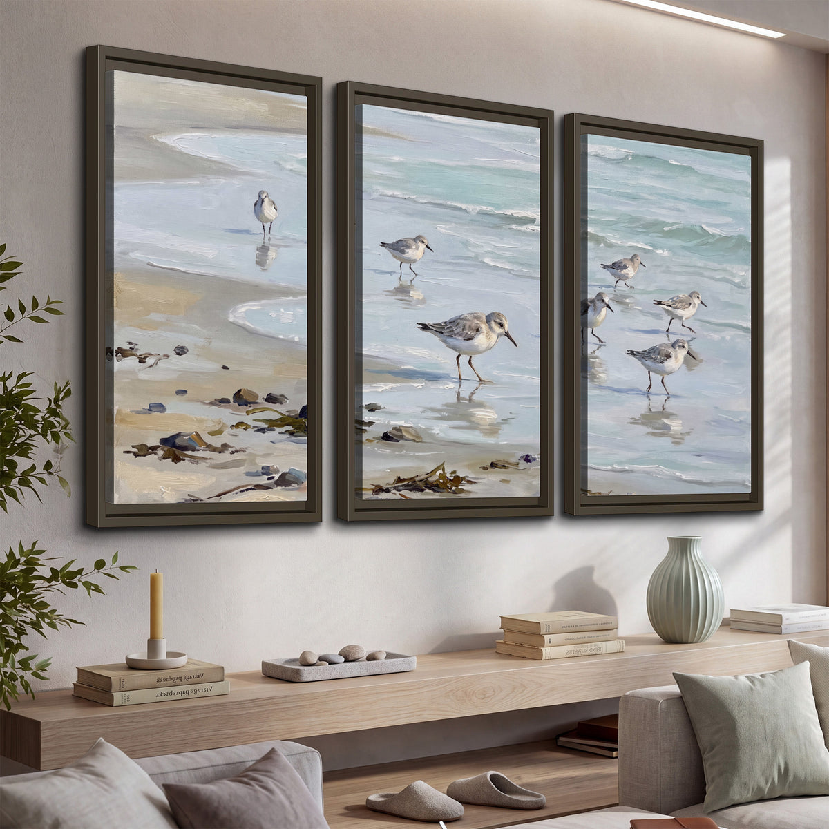 Small shorebirds standing along a pale blue shoreline 3 piece framed canvas wall art displayed in a console