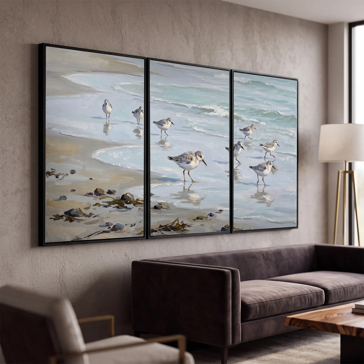 Small shorebirds standing along a pale blue shoreline 3 piece framed canvas wall art displayed in a modern living room