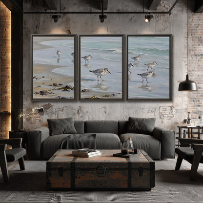 Small shorebirds standing along a pale blue shoreline 3 piece framed canvas wall art displayed in a industrial room