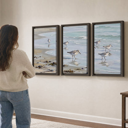Small shorebirds standing along a pale blue shoreline 3 piece framed canvas wall art three panel arrangement on a wall