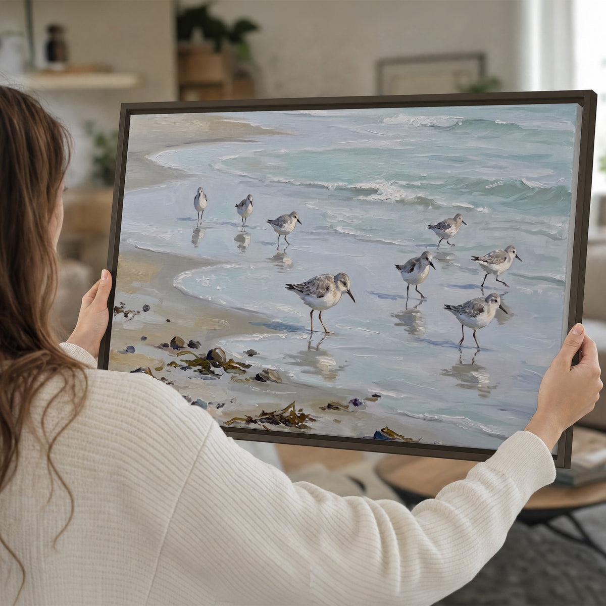 Small shorebirds standing along a pale blue shoreline single framed canvas wall art held in hands