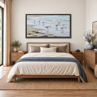 Small shorebirds standing along a pale blue shoreline single framed canvas wall art styled in an interior