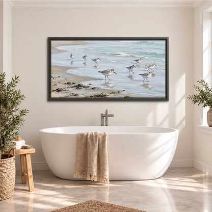 Small shorebirds standing along a pale blue shoreline single framed canvas wall art styled in an interior