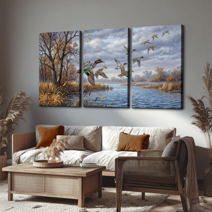 Ducks taking flight over a blue river framed by autumn branches 3 piece canvas wall art displayed in a rustic living room