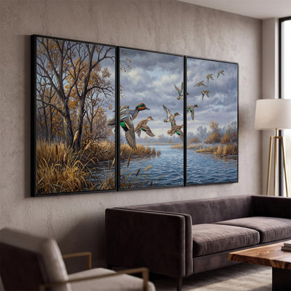 Ducks taking flight over a blue river framed by autumn branches 3 piece framed canvas wall art displayed in a modern living room