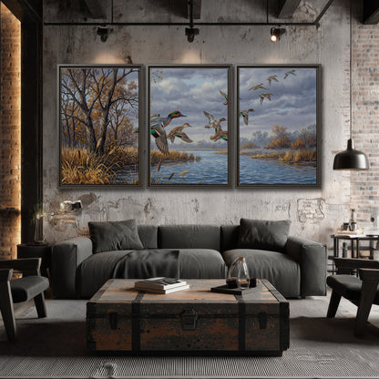 Ducks taking flight over a blue river framed by autumn branches 3 piece framed canvas wall art displayed in a industrial room