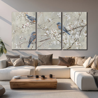 Bluebirds perched on delicate white flowering branches against pale sage 3 piece canvas wall art displayed in a living room