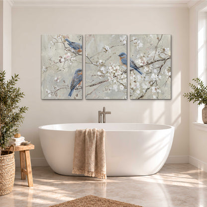 Bluebirds perched on delicate white flowering branches against pale sage 3 piece canvas wall art styled in an interior