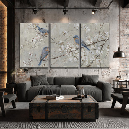 Bluebirds perched on delicate white flowering branches against pale sage 3 piece canvas wall art displayed in a industrial room