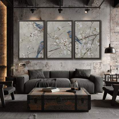 Bluebirds perched on delicate white flowering branches against pale sage 3 piece framed canvas wall art displayed in a industrial room