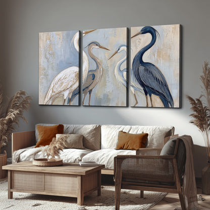 Three long-necked herons in soft ivory and dark blue against pale blue-gray 3 piece canvas wall art displayed in a rustic living room