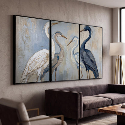Three long-necked herons in soft ivory and dark blue against pale blue-gray 3 piece framed canvas wall art displayed in a modern living room