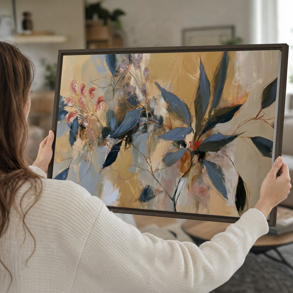 Layered navy leaves and muted pink blossoms against a golden cream background single framed canvas wall art held in hands