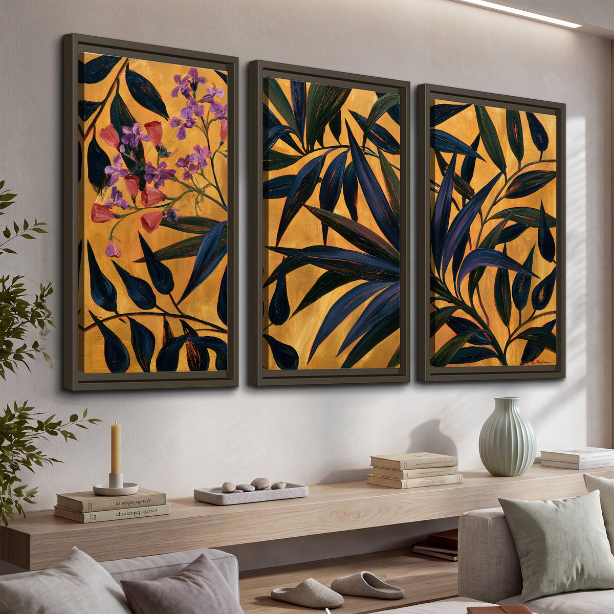 Dark pointed bamboo leaves across an ochre background with small pink floral accents 3 piece framed canvas wall art displayed in a console