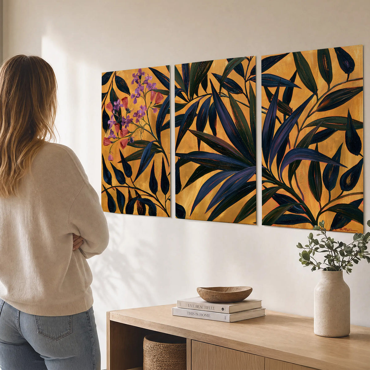 Dark pointed bamboo leaves across an ochre background with small pink floral accents set of 3 poster prints three panel arrangement on a wall