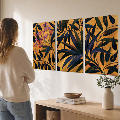 Dark pointed bamboo leaves across an ochre background with small pink floral accents set of 3 poster prints three panel arrangement on a wall