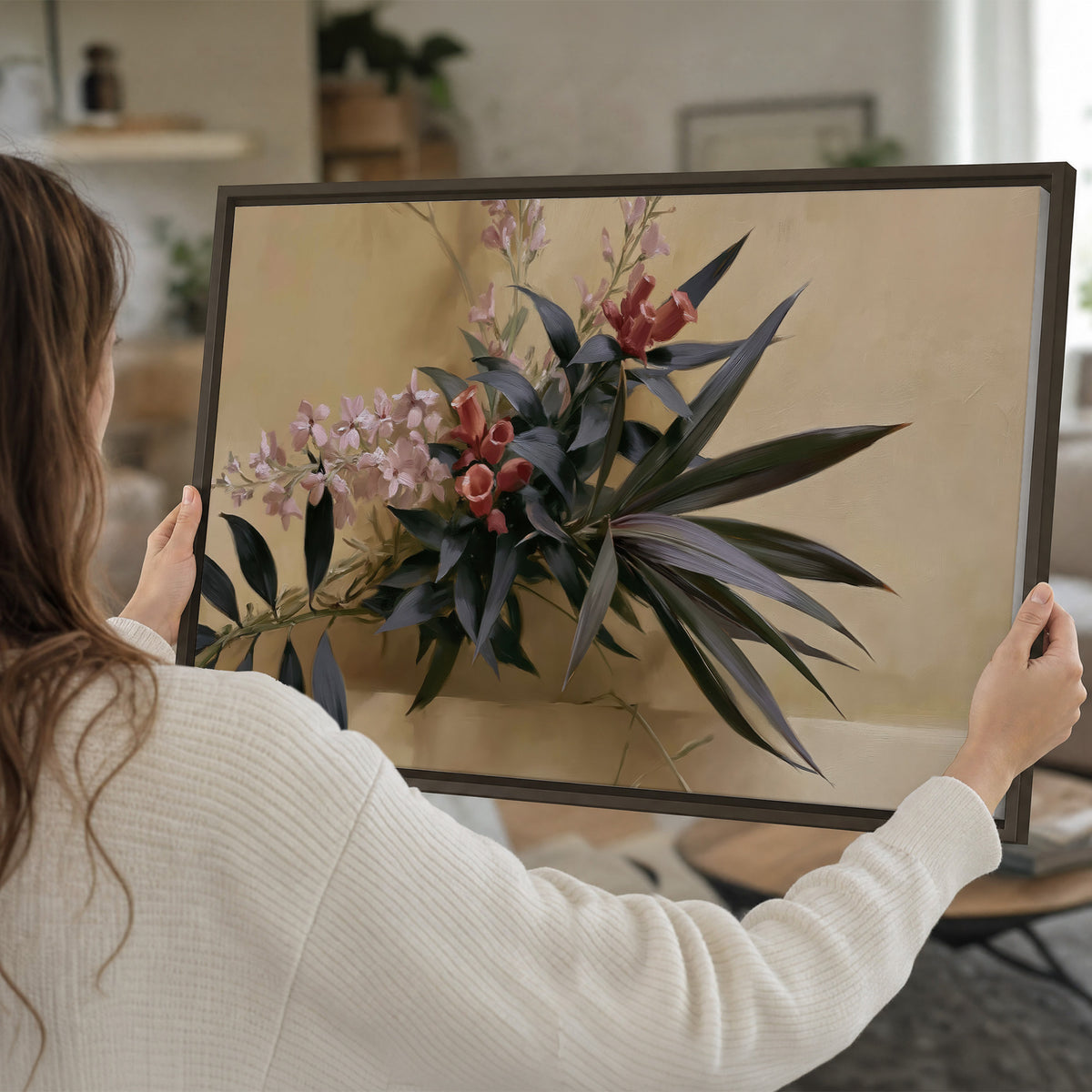 Long dark leaves and dusty pink flowers arranged against a soft beige background single framed canvas wall art held in hands