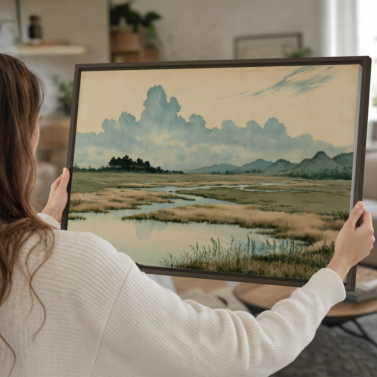 A calm marshland with reflective pools and distant blue-green hills under a clouded sky single framed canvas wall art held in hands